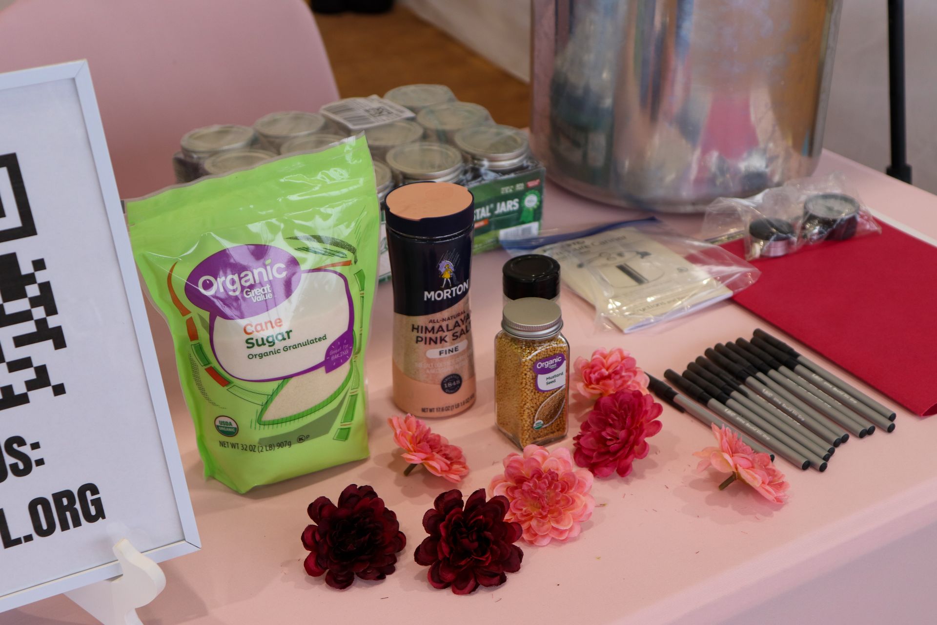 A table with a bag of sugar , a bottle of coffee , and flowers on it.