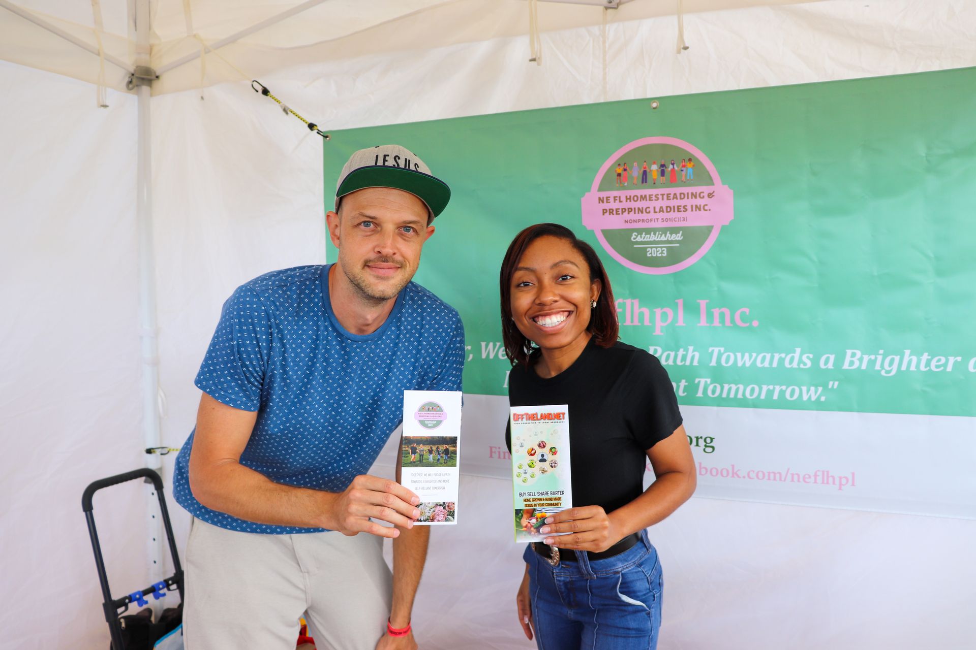A man and a woman are standing under a tent holding brochures.