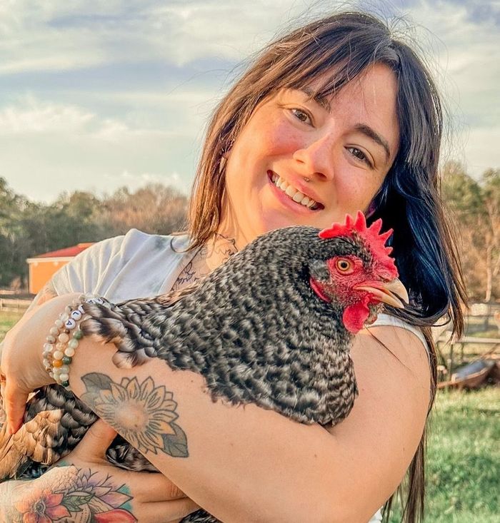 A woman is holding a chicken in her arms and smiling.