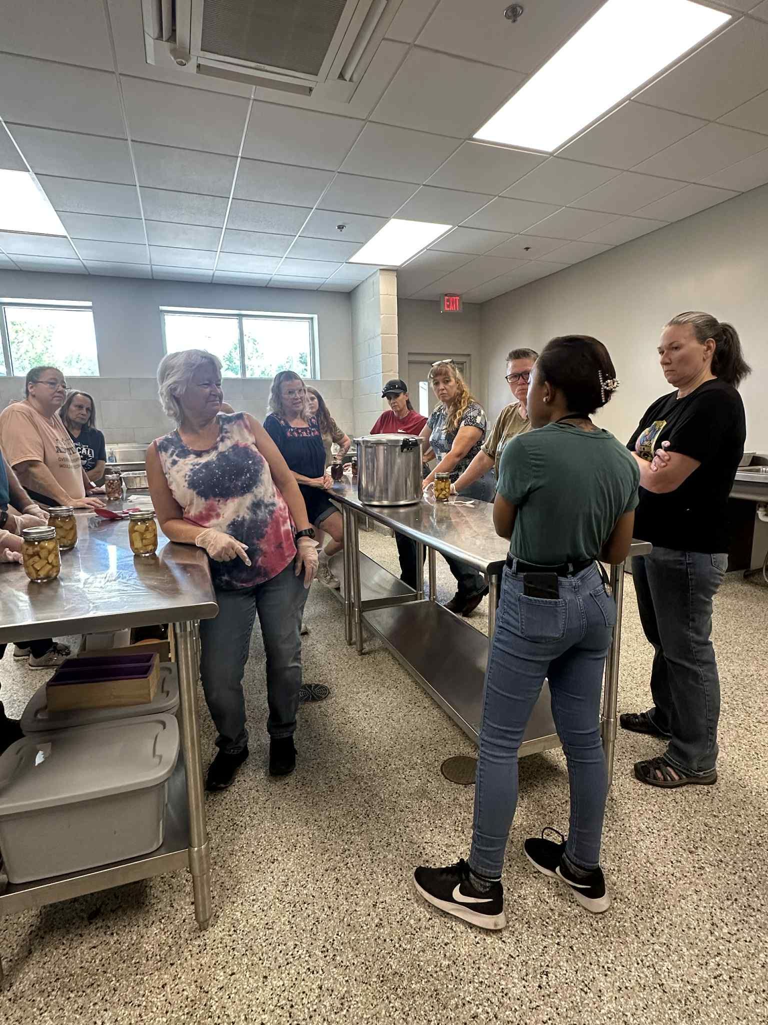 A group of people are standing around tables in a kitchen.