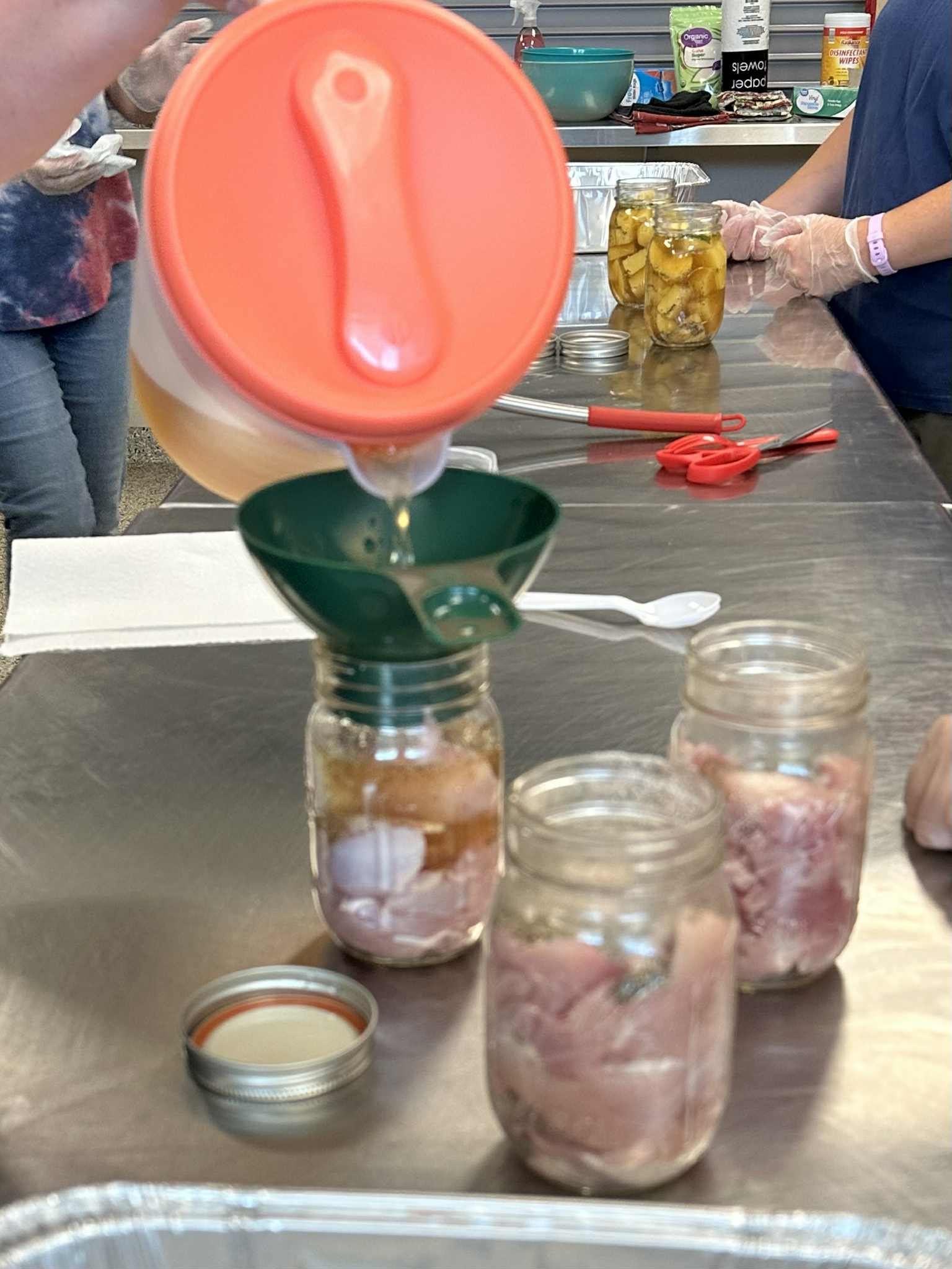 A person pouring liquid into a jar with a funnel