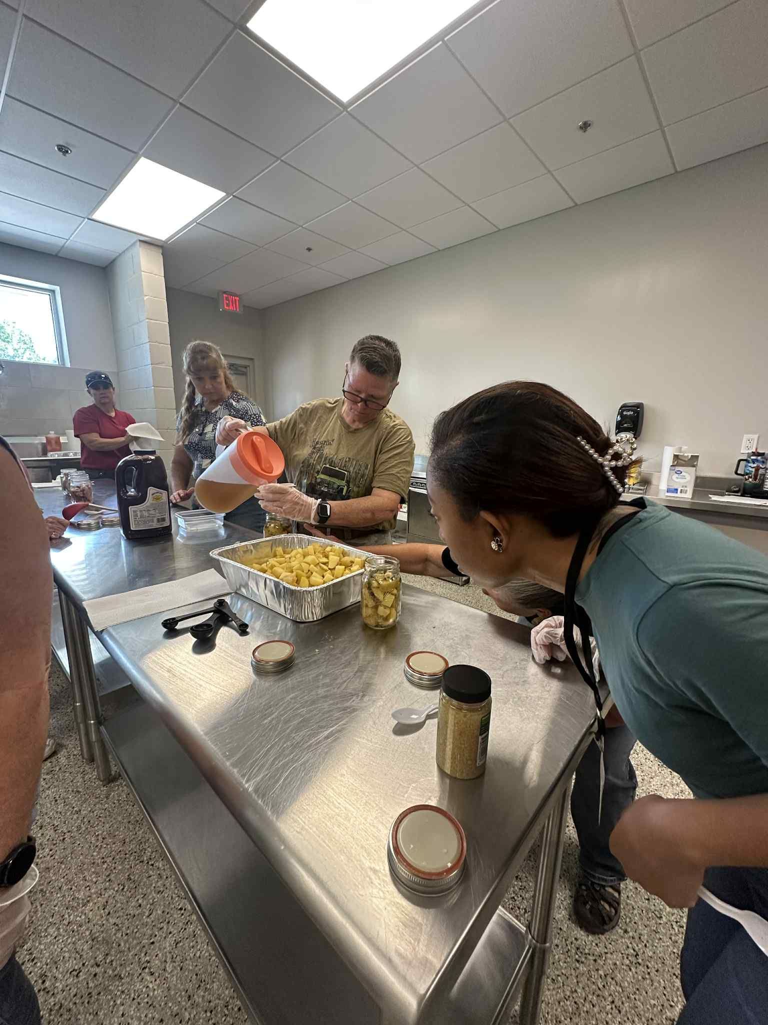 A group of people are standing around a table in a kitchen preparing food.