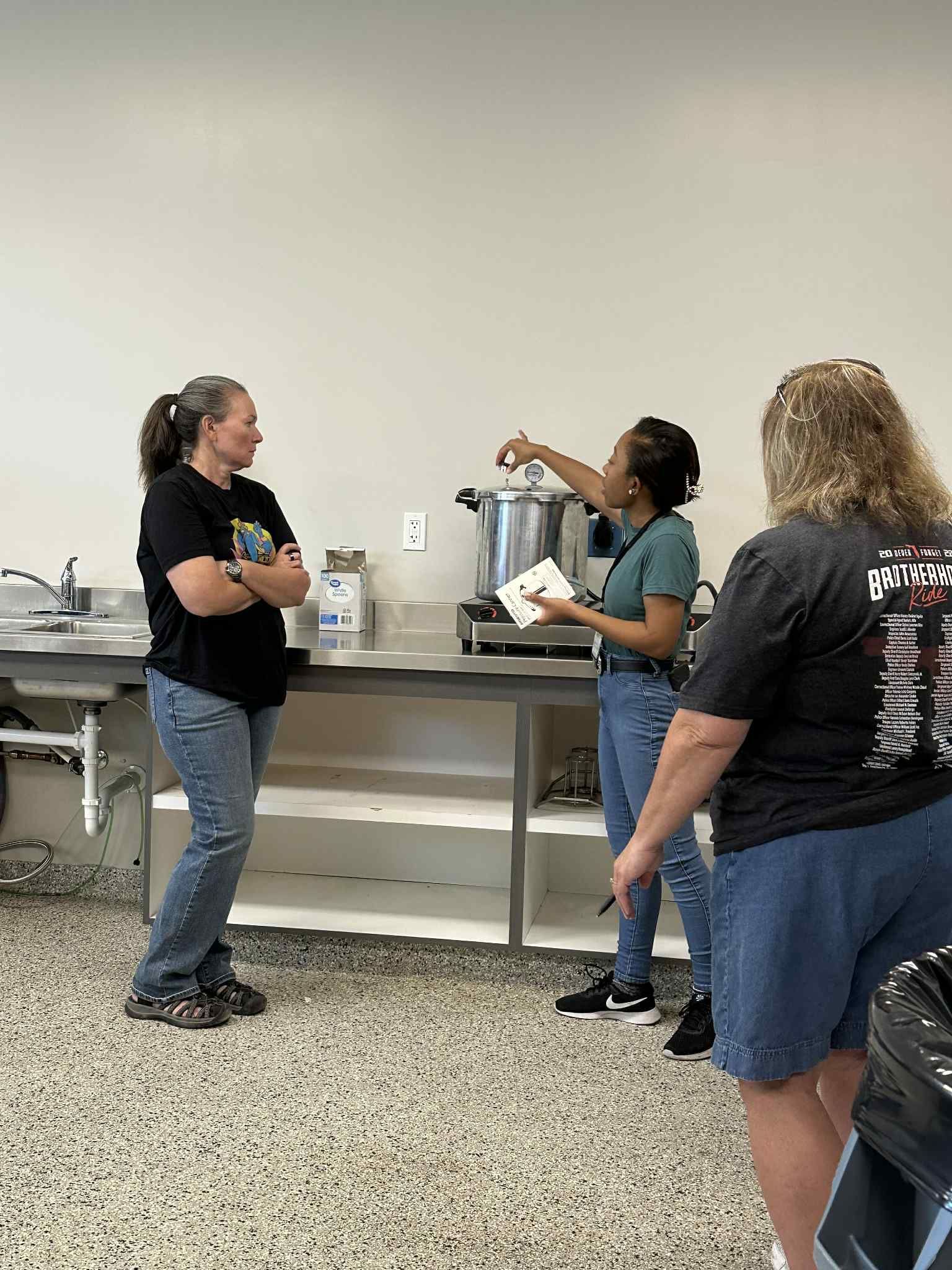 A group of women are standing in a kitchen talking to each other.