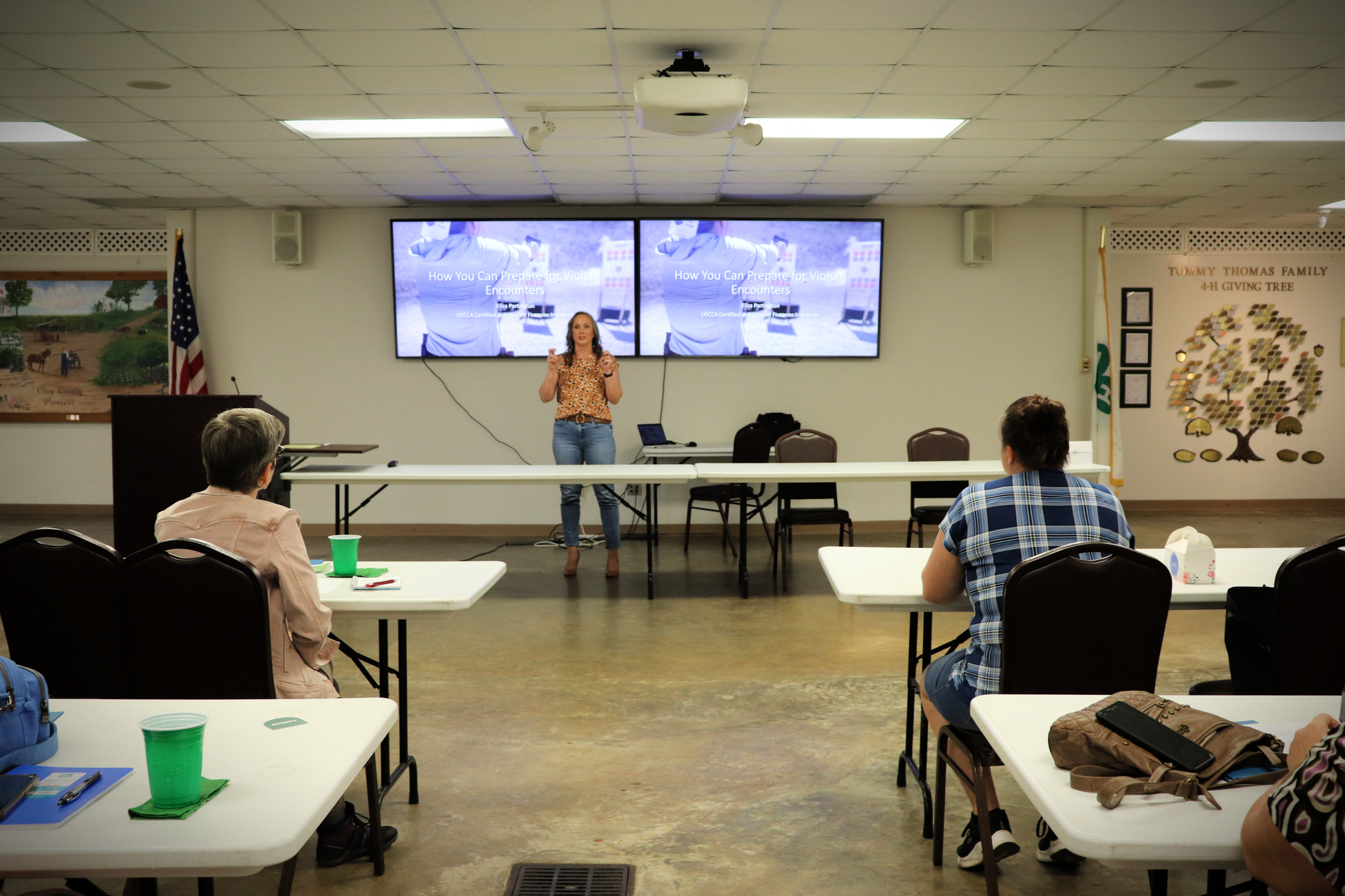 A woman is giving a presentation to a group of people sitting at tables.