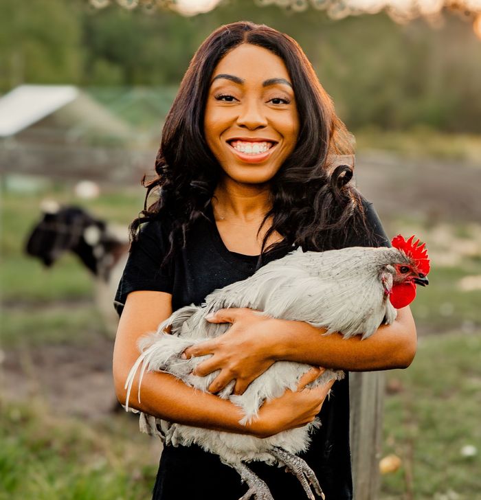 A woman is holding a rooster in her arms and smiling.