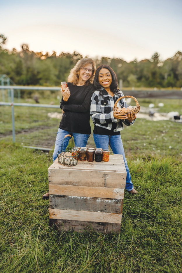 Two women are standing next to each other in a field holding jars.