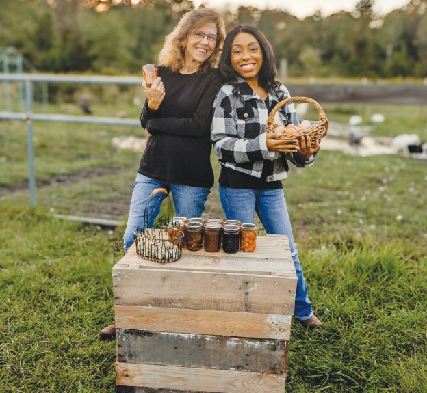 Two women are standing next to each other in a field holding baskets of food.