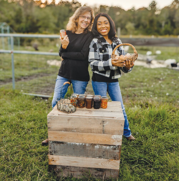 Two women are standing next to each other in a field holding jars.