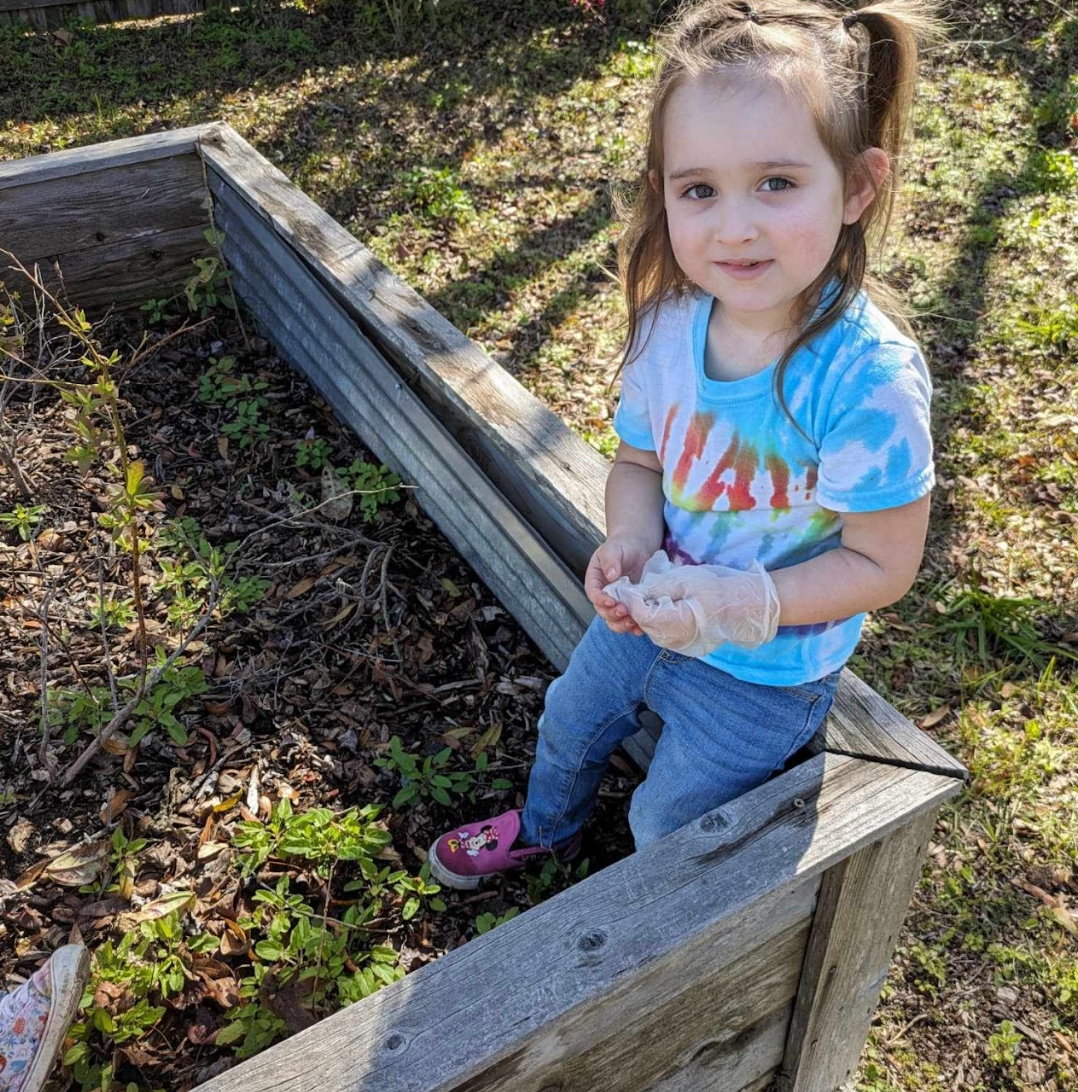 A little girl is sitting in a wooden box in the grass.