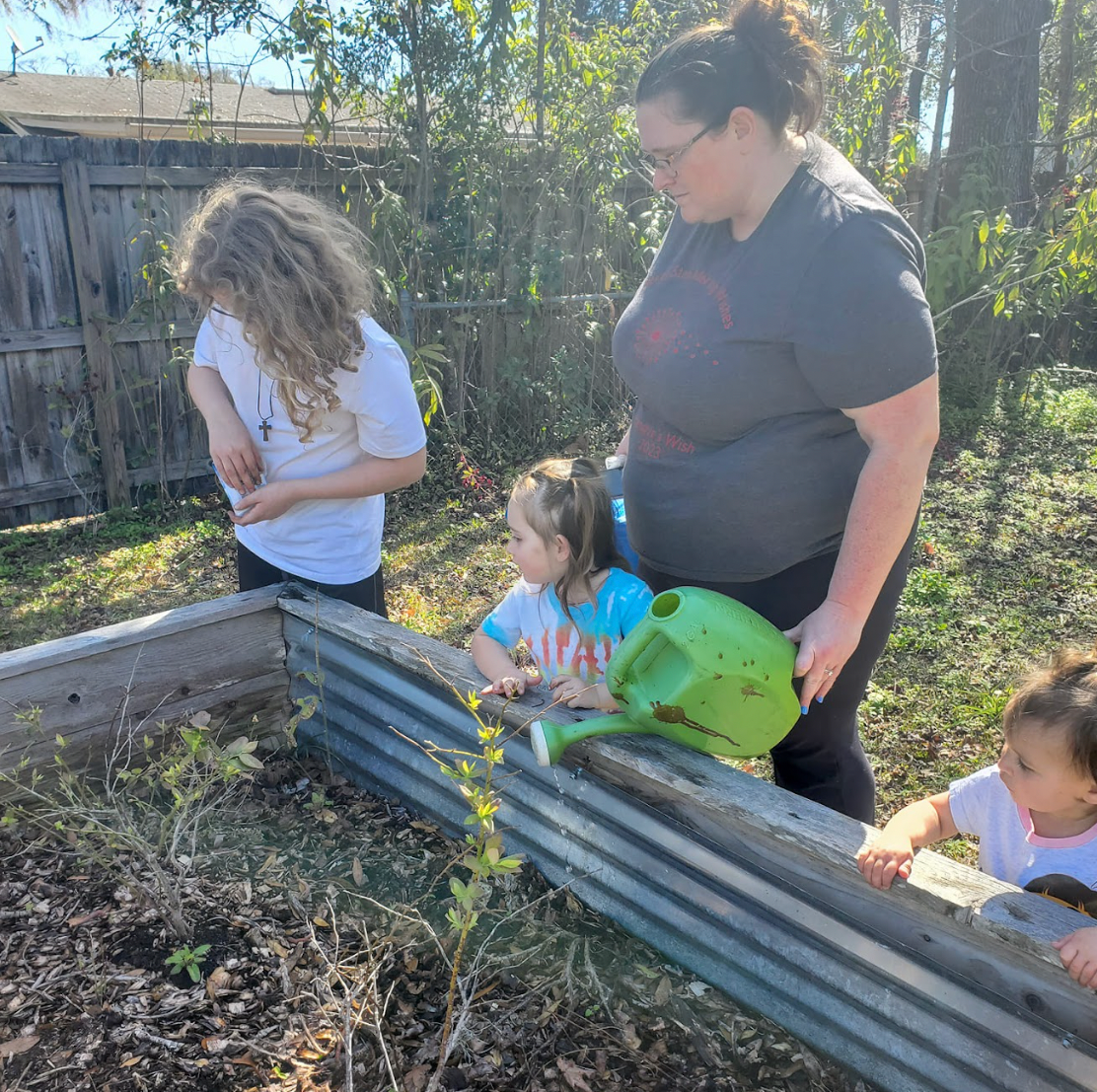 A woman and two children are watering plants in a garden.