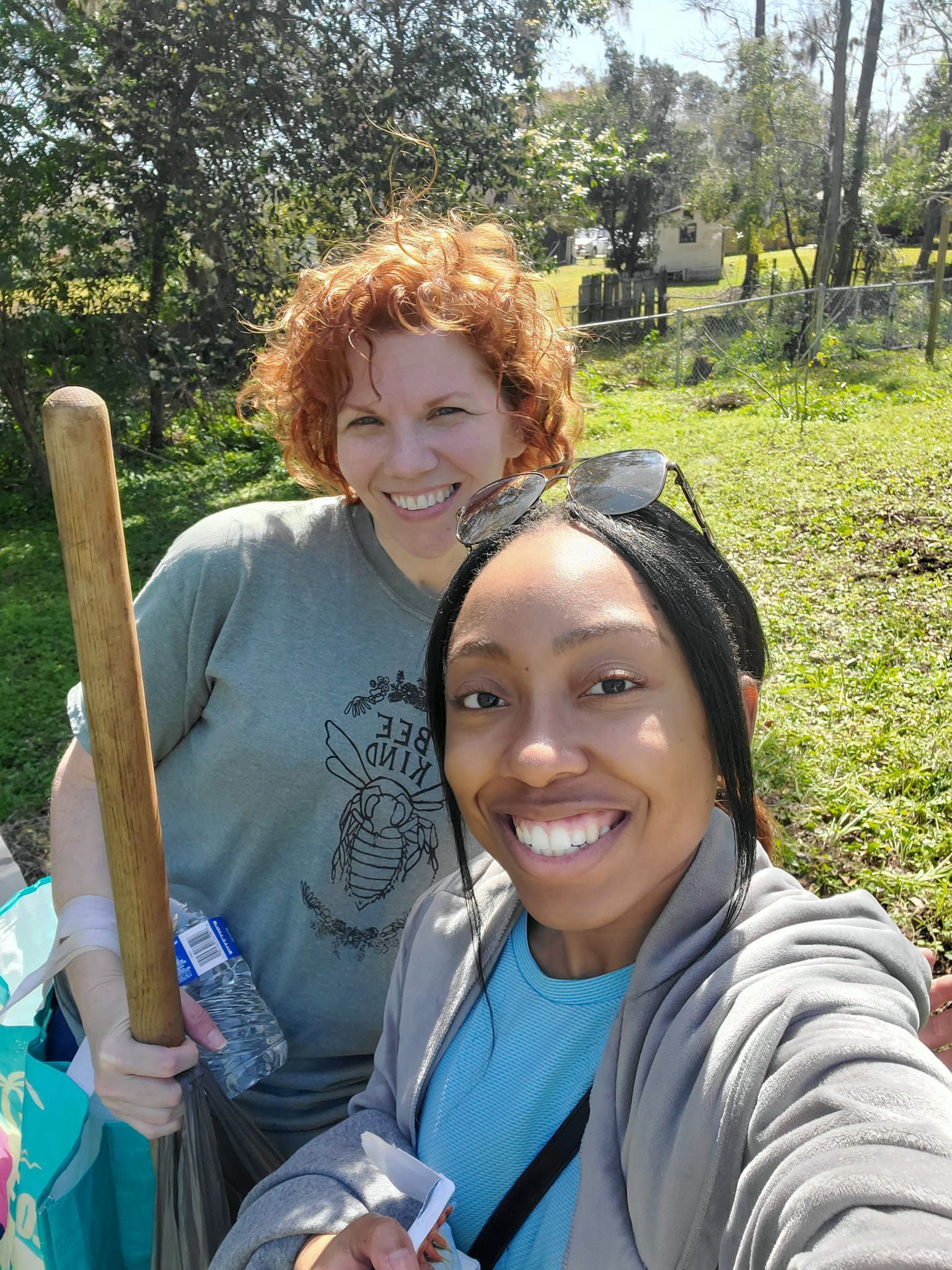 Two women are standing next to each other in a field holding a wooden stick.