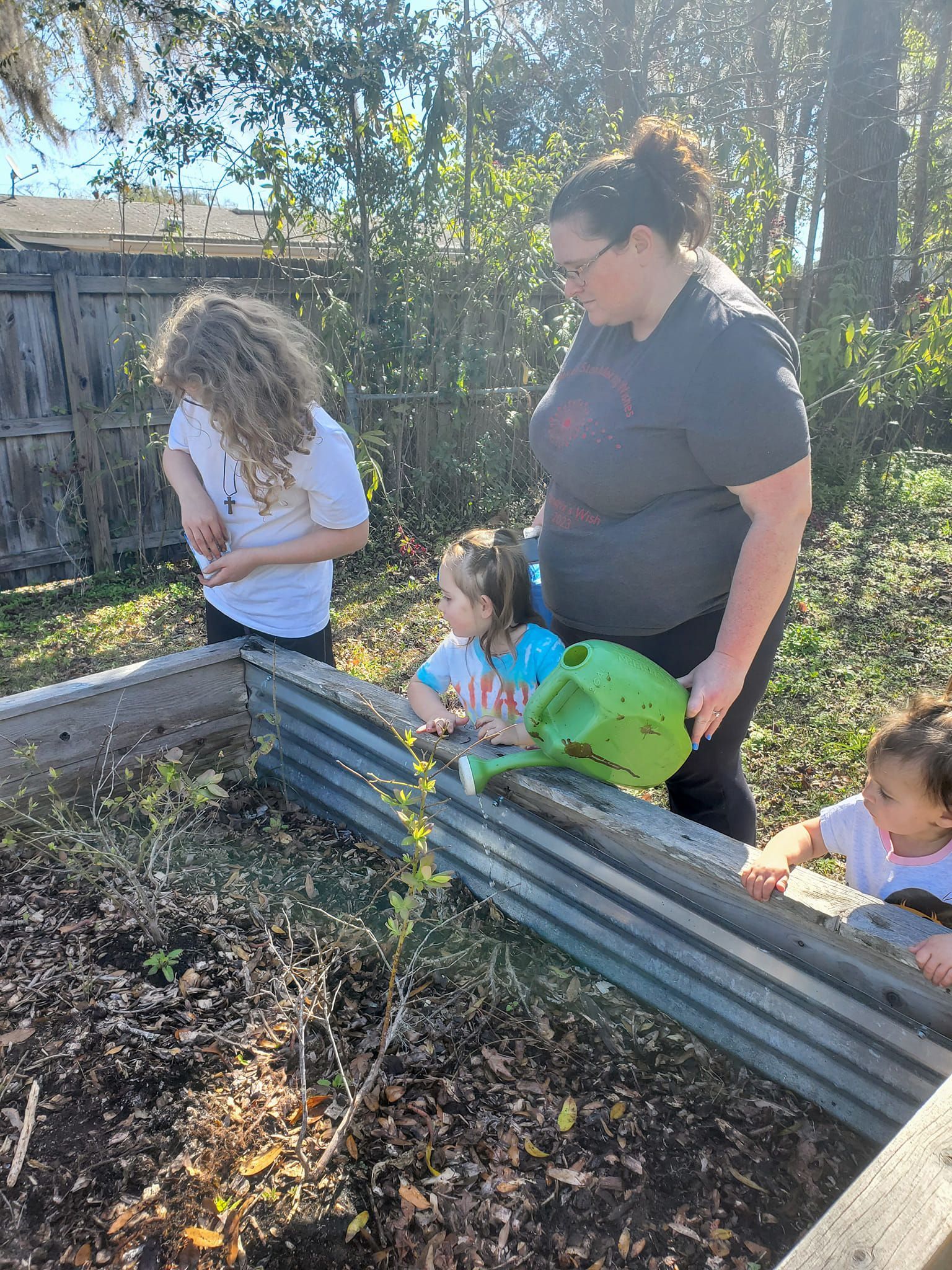 A woman is watering plants in a garden with two children.