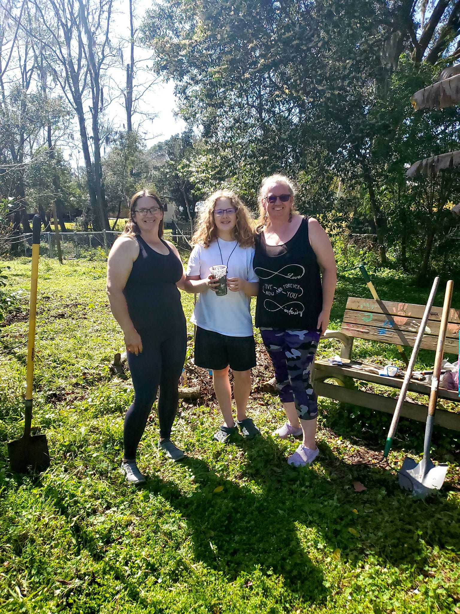 Three women are standing next to each other in a grassy field.