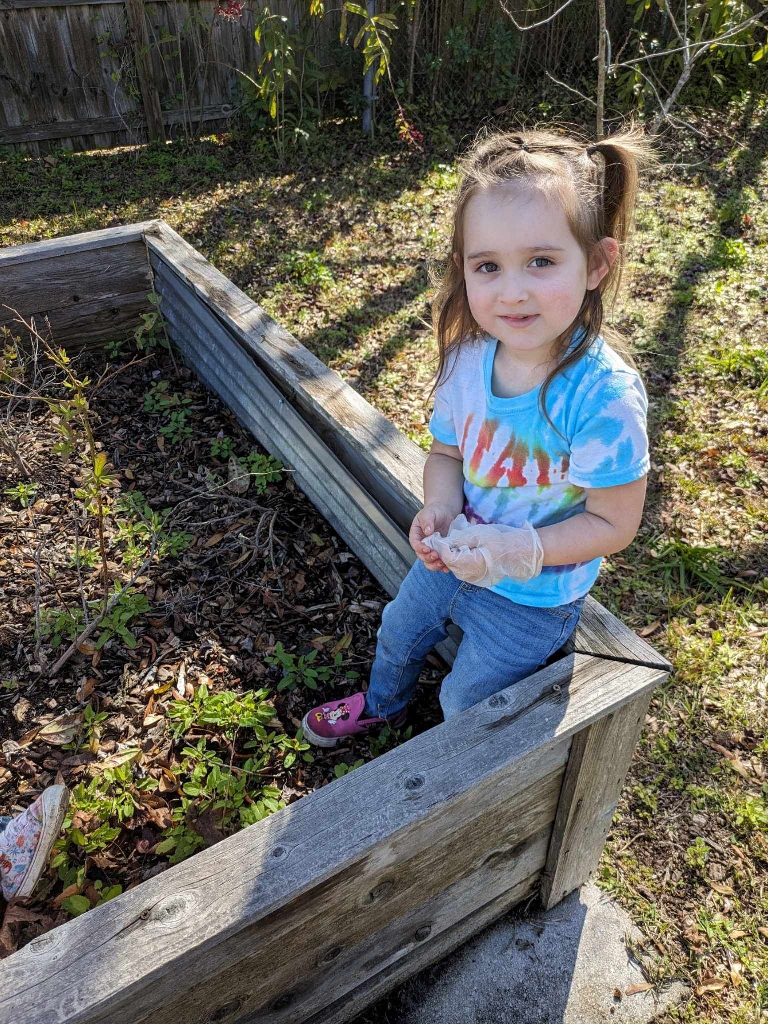 A little girl is sitting in a wooden box in a garden.