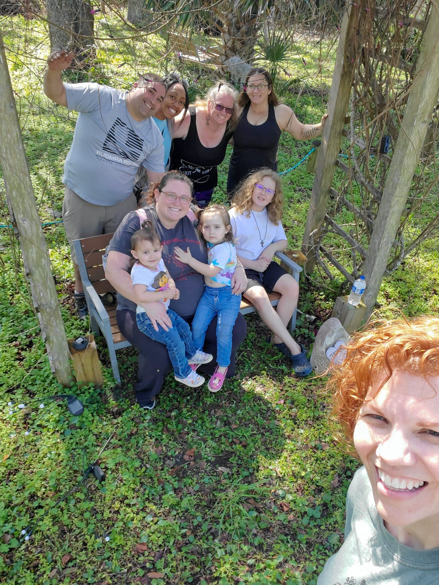 A group of people are sitting on a bench in the grass.