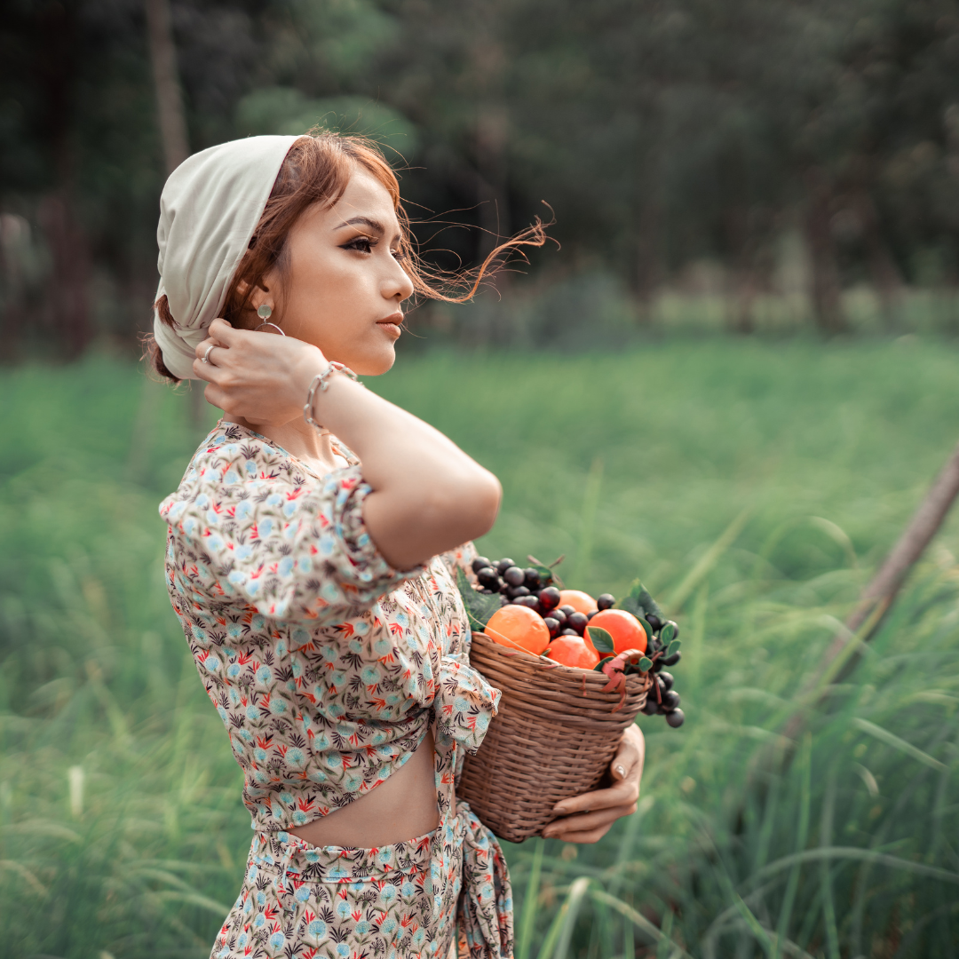 A woman is holding a basket of fruit in a field.