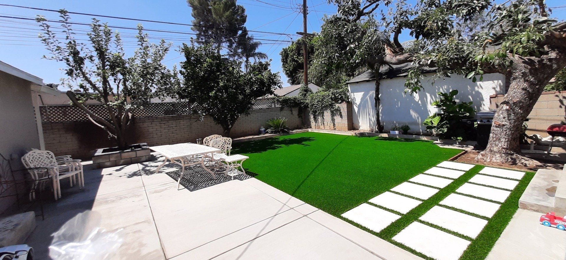 a back yard with stepping stones, new concrete and synthetic grass