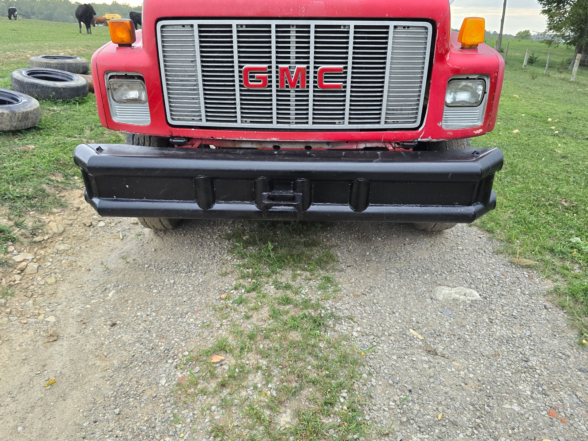 A red gmc truck is parked on a gravel road.