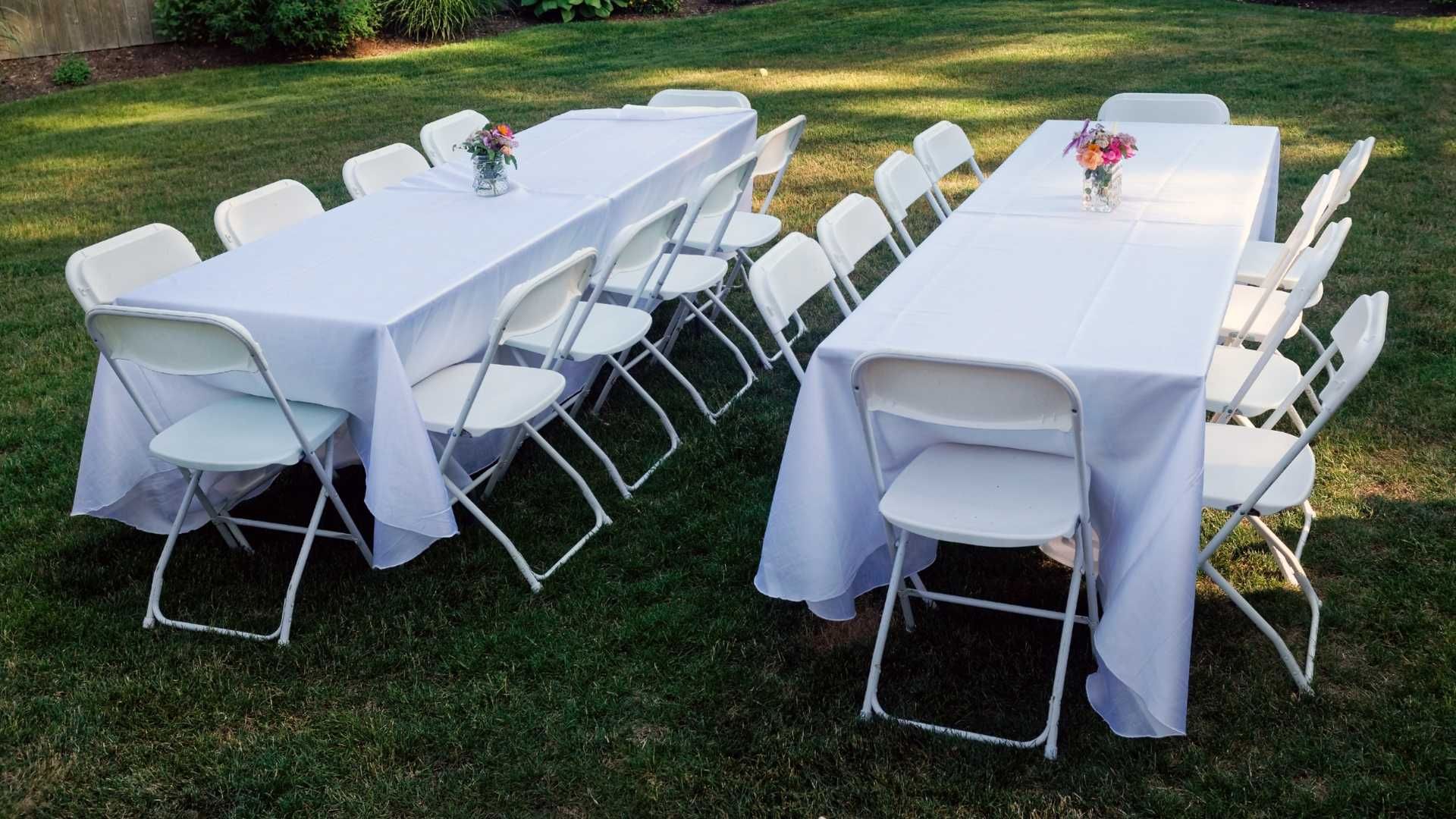 A row of white folding chairs and tables on a lush green field.