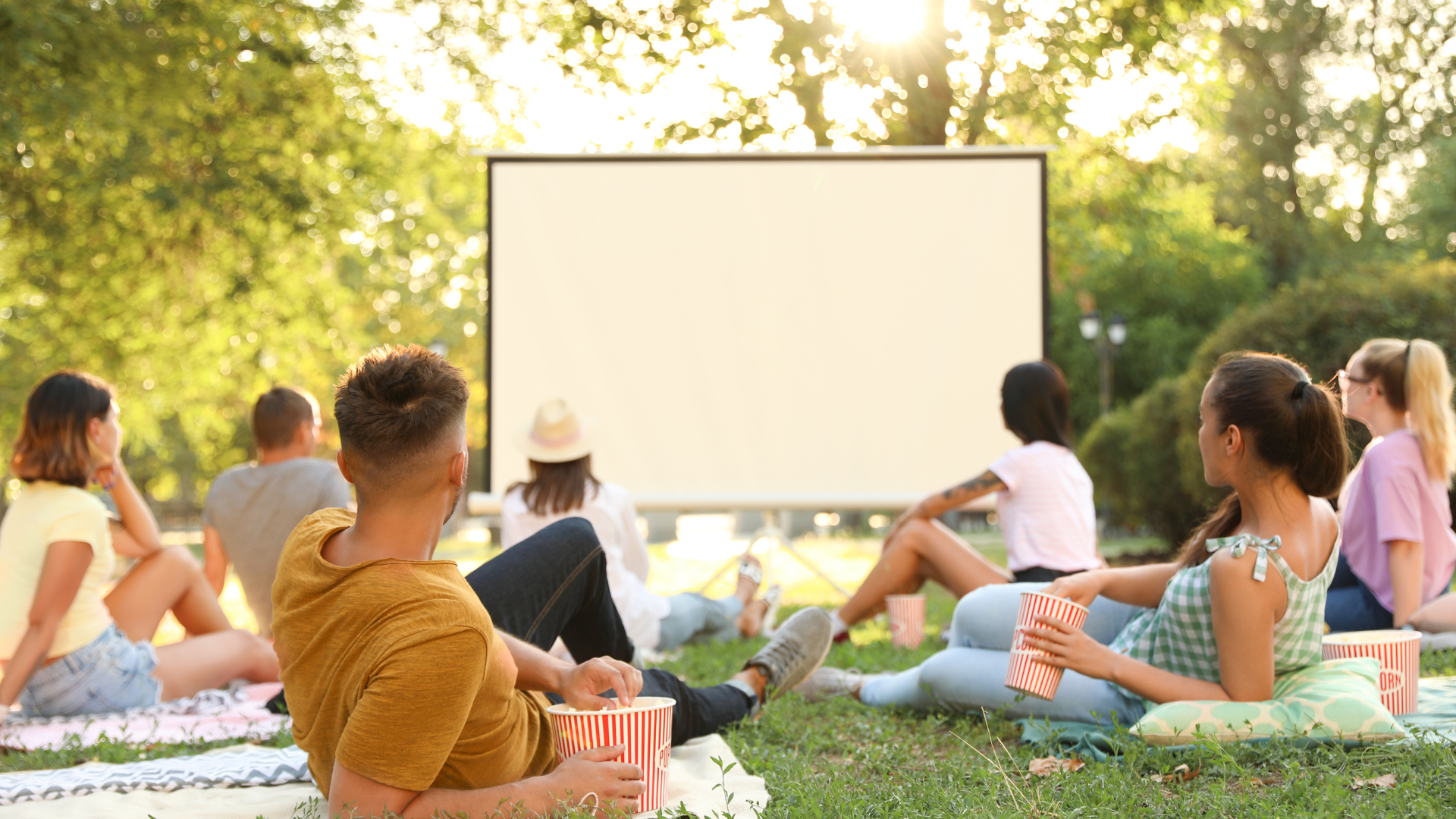 A group of people are sitting on the grass watching a movie on a large screen.