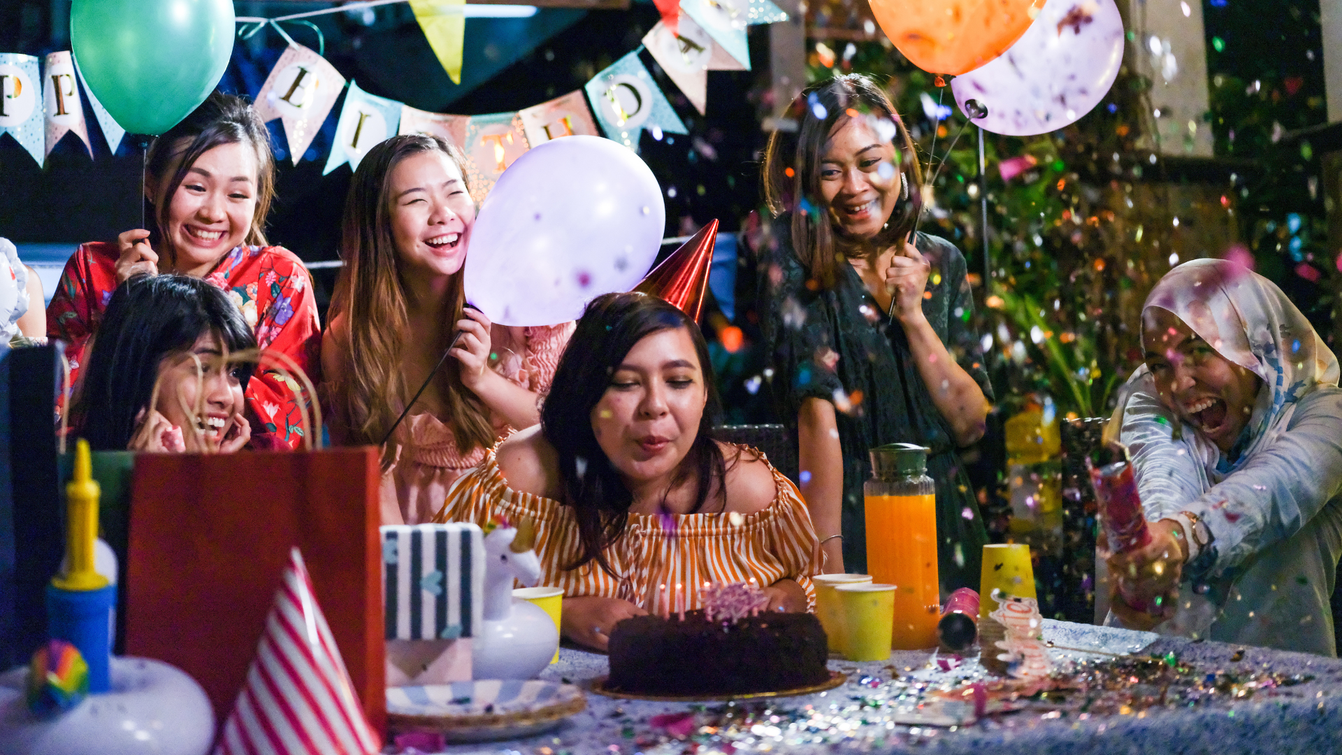 A group of women are celebrating a birthday with balloons and confetti.