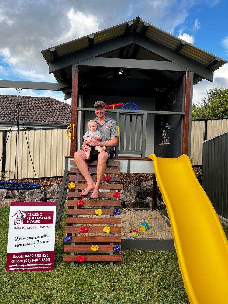 Man Is Holding A Baby While Sitting On A Slide — Builder In Gympie, QLD