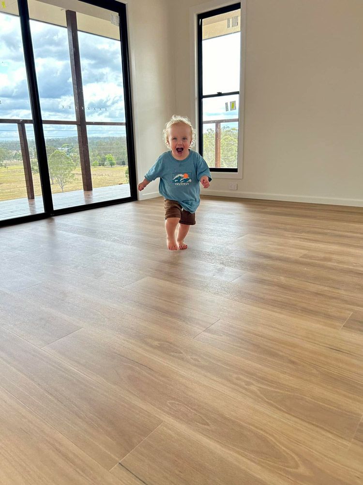 Little Boy Is Walking On A Wooden Floor In An Empty Room — Builder In Gympie, QLD