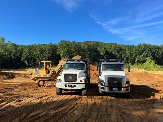 Two dump trucks are parked next to each other on a dirt road.