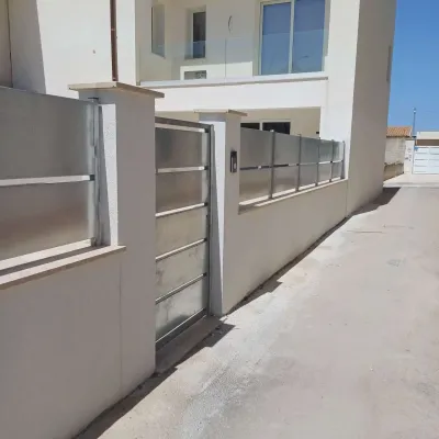 Una casa moderna con cancello in metallo e recinzione in vetro smerigliato. Pareti bianche, giornata di sole.