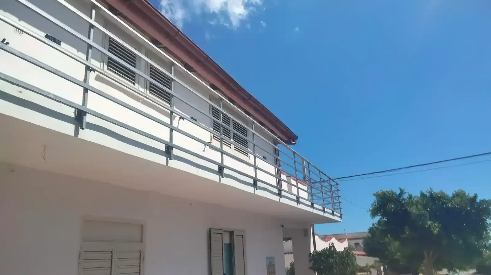 Edificio bianco con balcone, ringhiera in metallo, cielo azzurro.