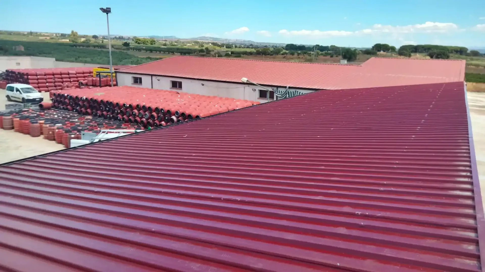 Tetti rossi in lamiera ondulata sugli edifici e tubi accatastati all'esterno, cielo azzurro.