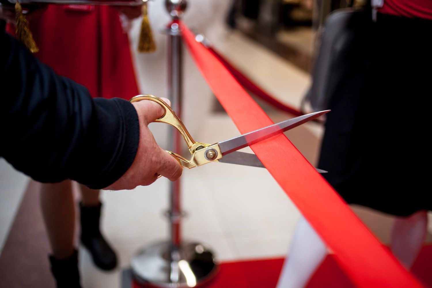 A person is cutting a red ribbon with scissors.