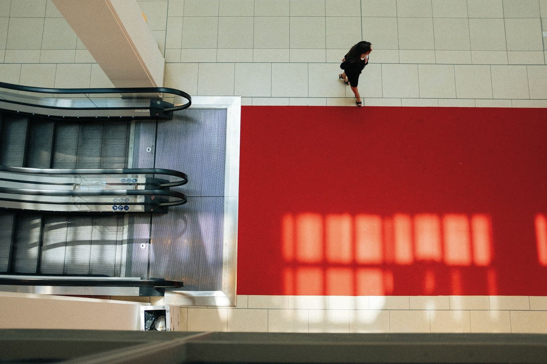 A person standing on a red carpet next to an escalator