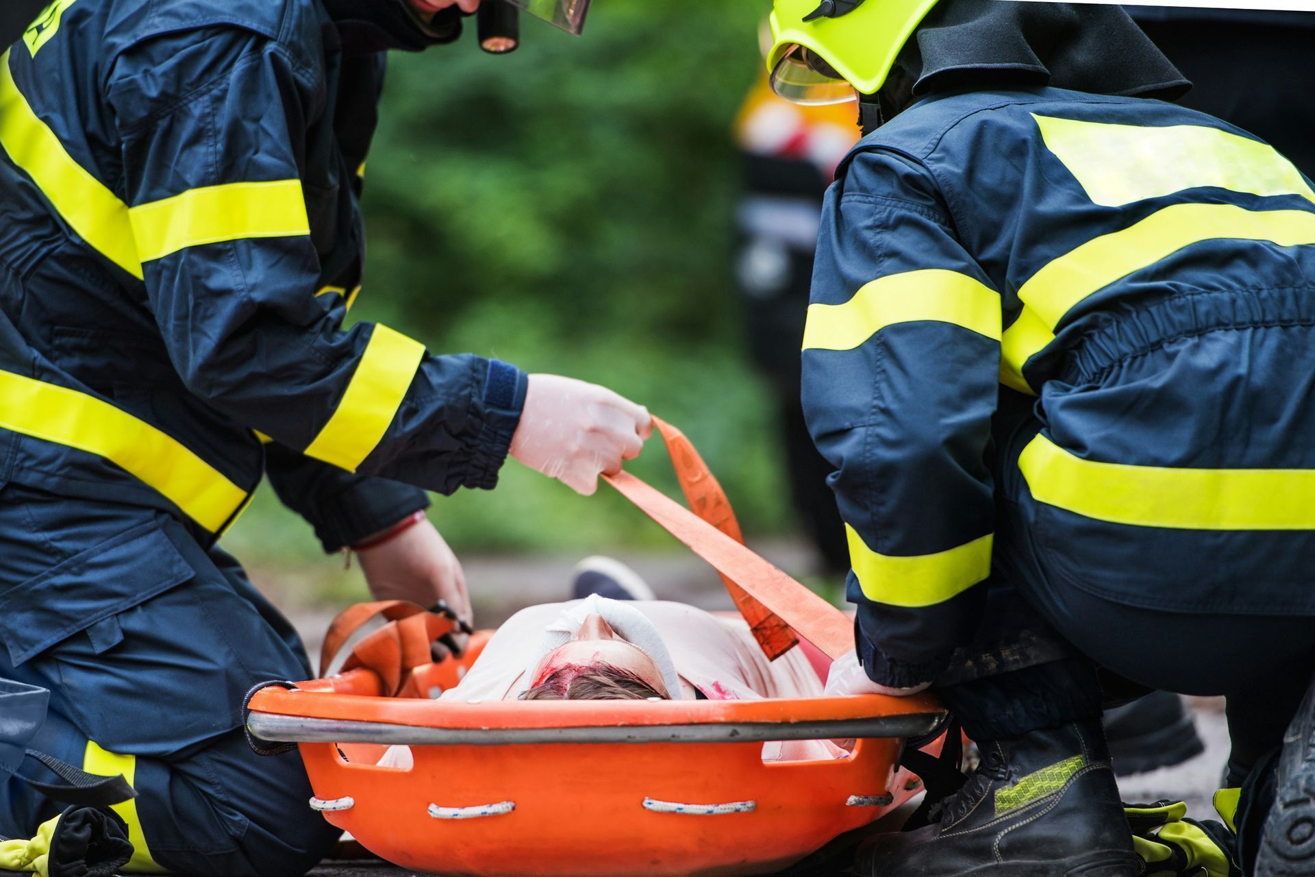 Two firefighters are kneeling down next to a stretcher with a person in it.