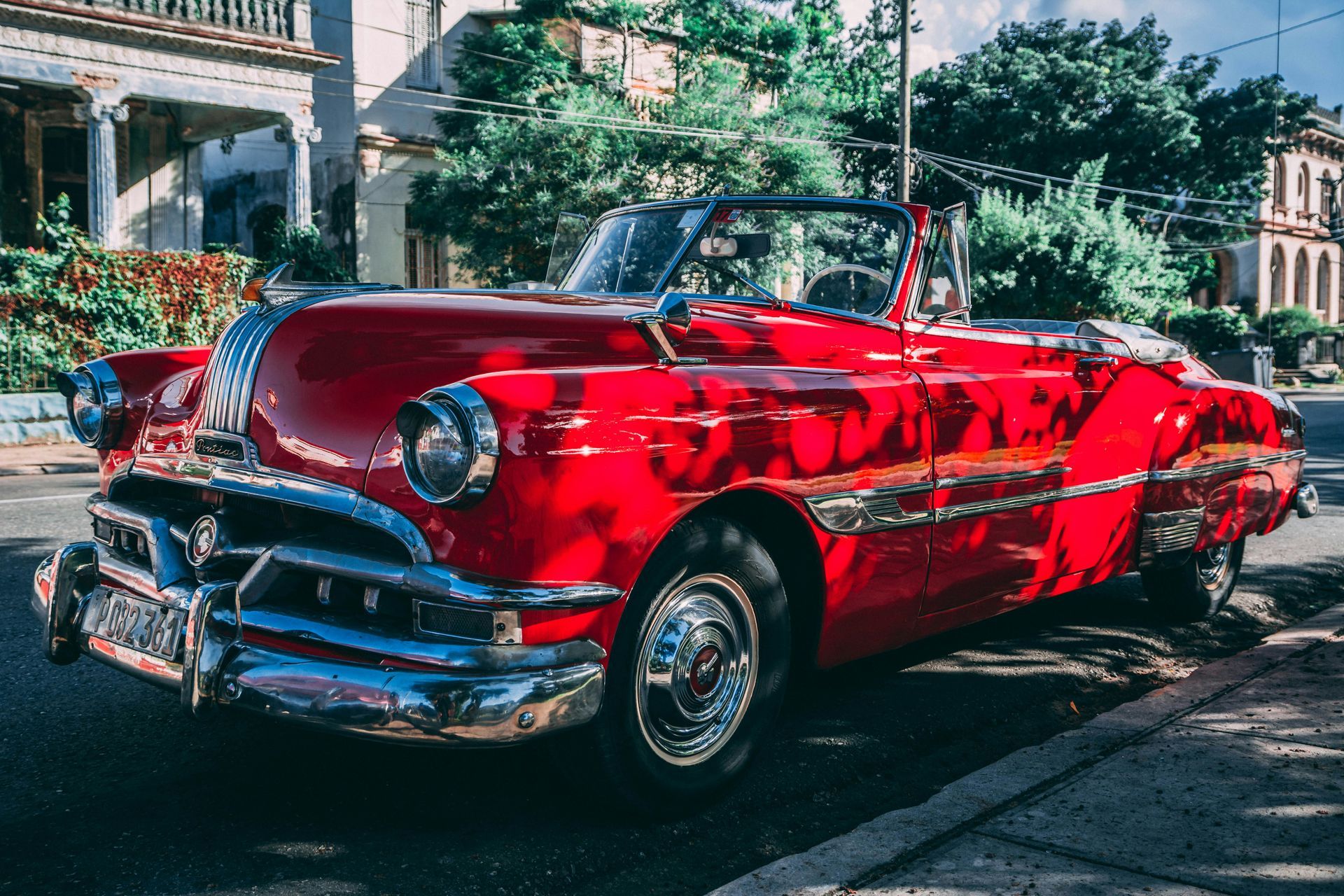 An old red convertible car is parked on the side of the road.