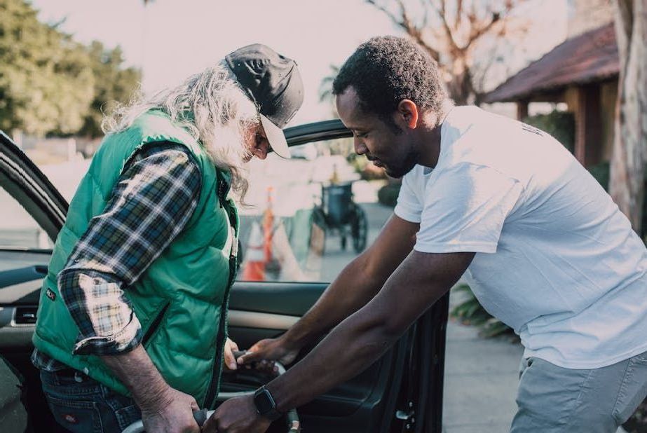 A man is helping an older man get into a car.