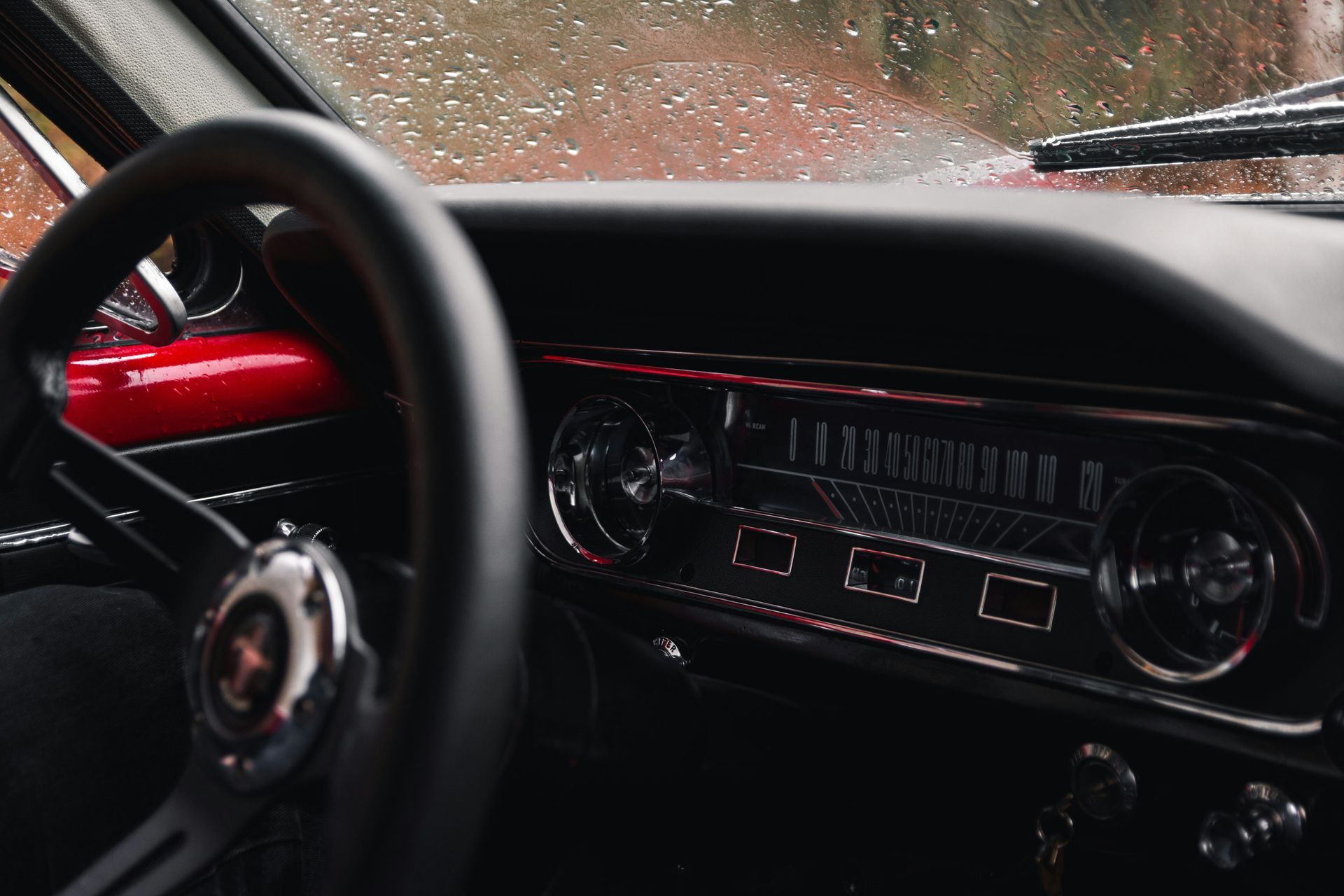 A close up of a steering wheel and dashboard of a car in the rain.