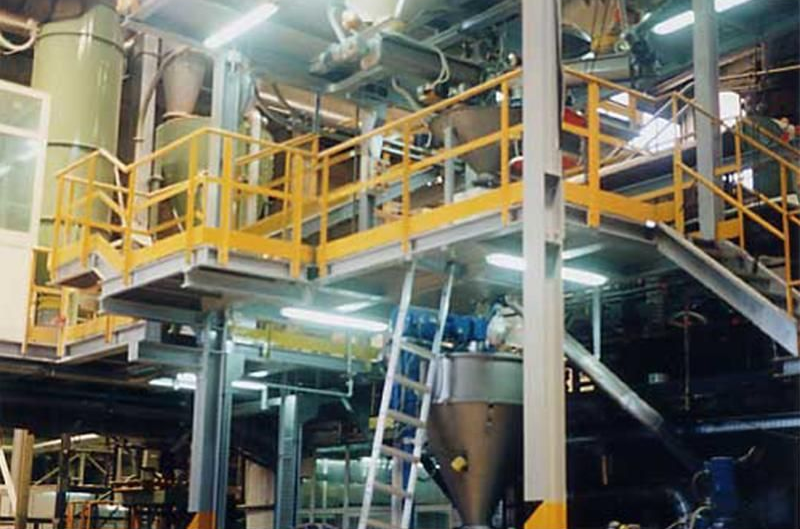 Piattaforma industriale con ringhiera gialla, macchinari grigi e una scala.