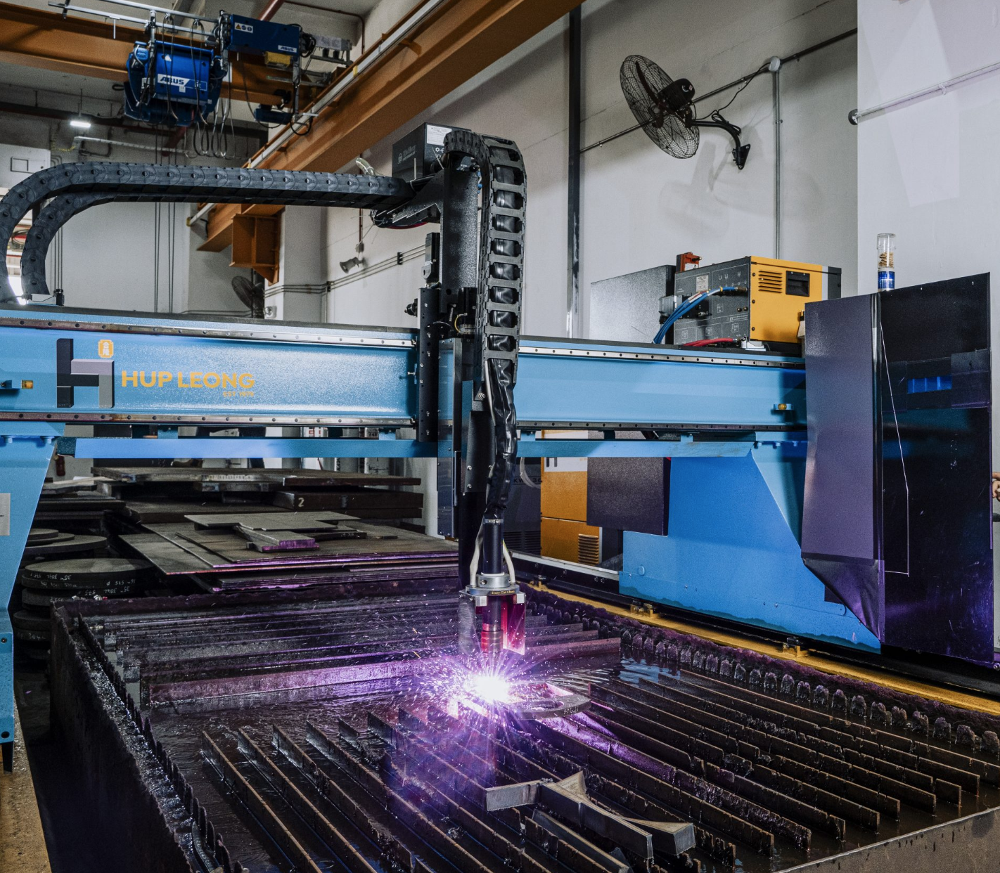 Un grande taglierino al plasma CNC blu in una fabbrica; le scintille volano mentre taglia lamiere.