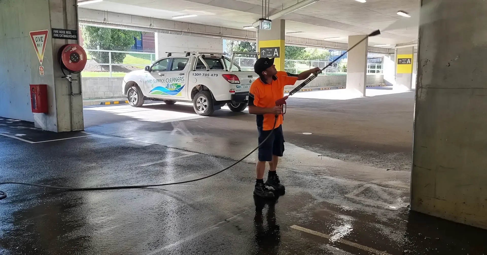 A Man Is Using a High Pressure Washer to Clean a Parking Garage — Hard Surface Cleaners in Sydney, NSW
