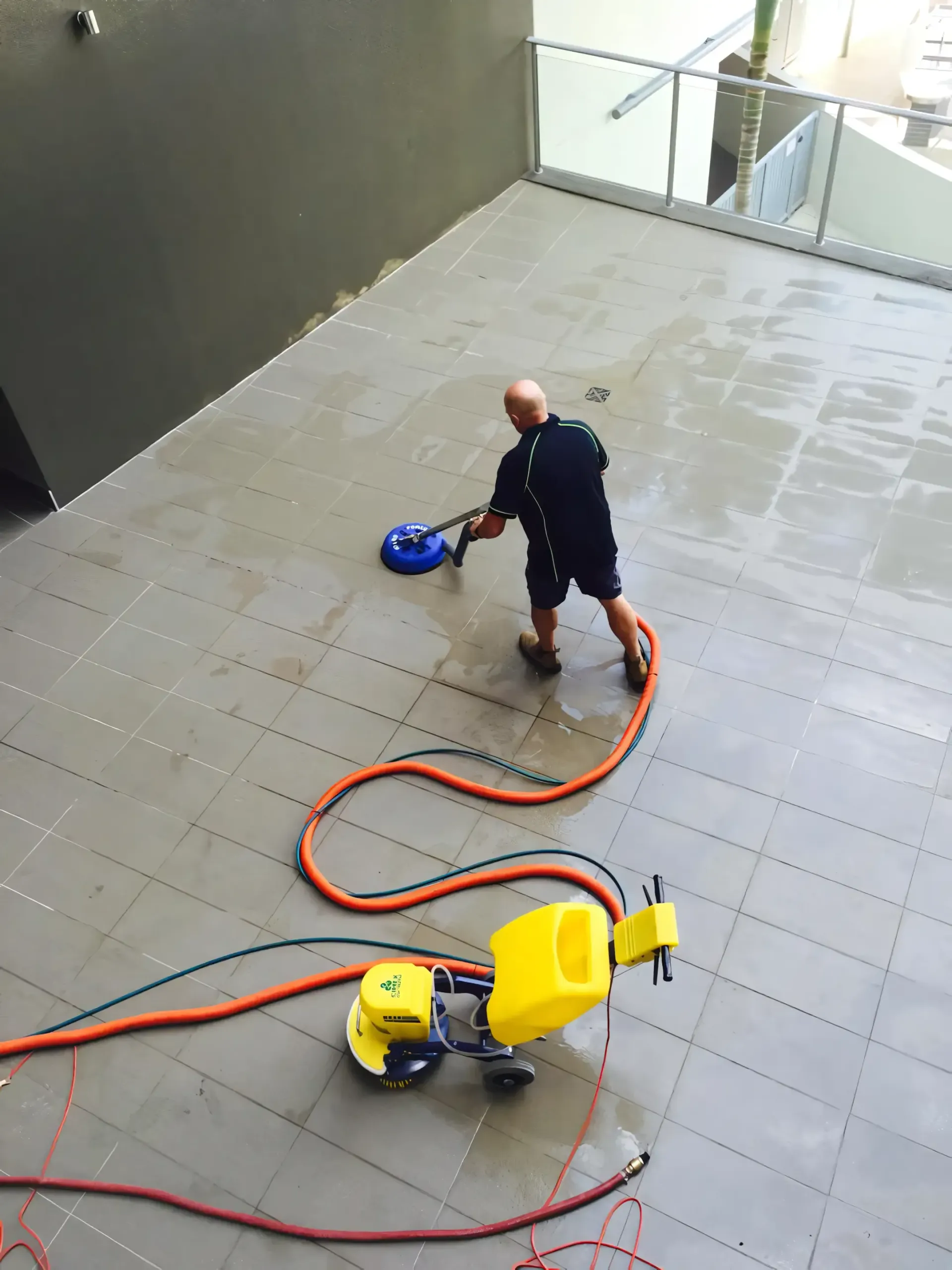 A man is cleaning a tiled floor with a hose — Hard Surface Cleaners in Gold Coast, QLD