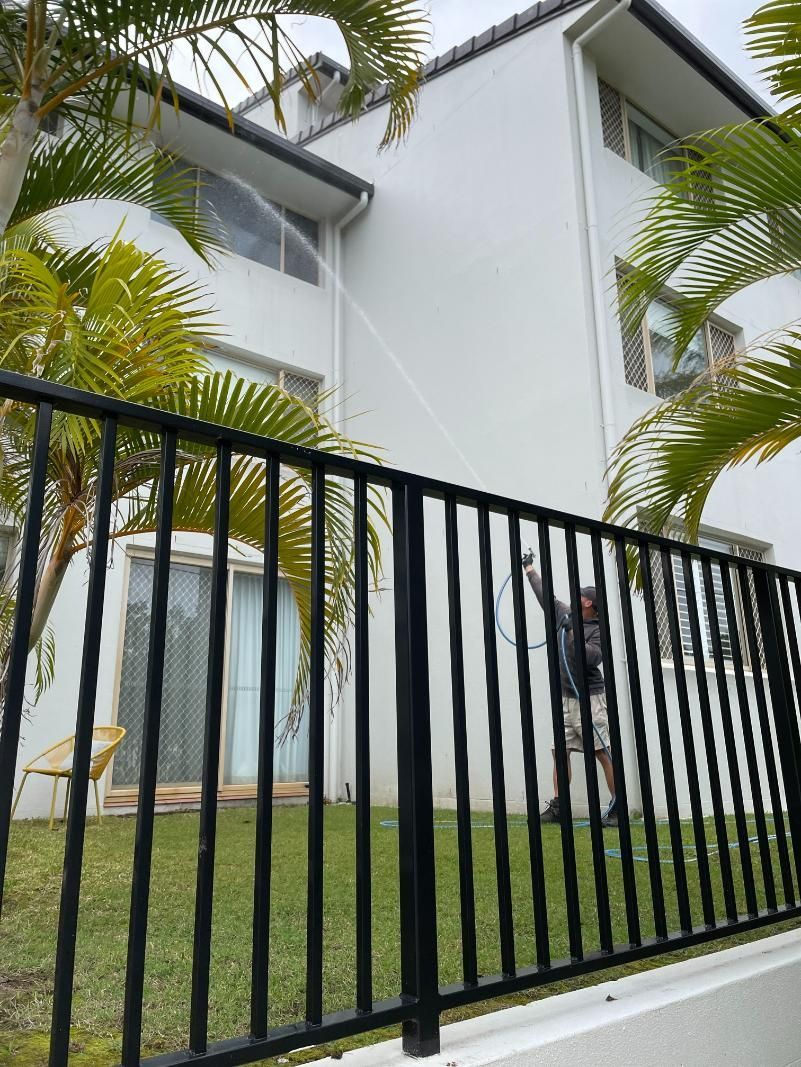 A Man Is Spraying Water on A Fence in Front of A House — Hard Surface Cleaners in Melbourne, VIC