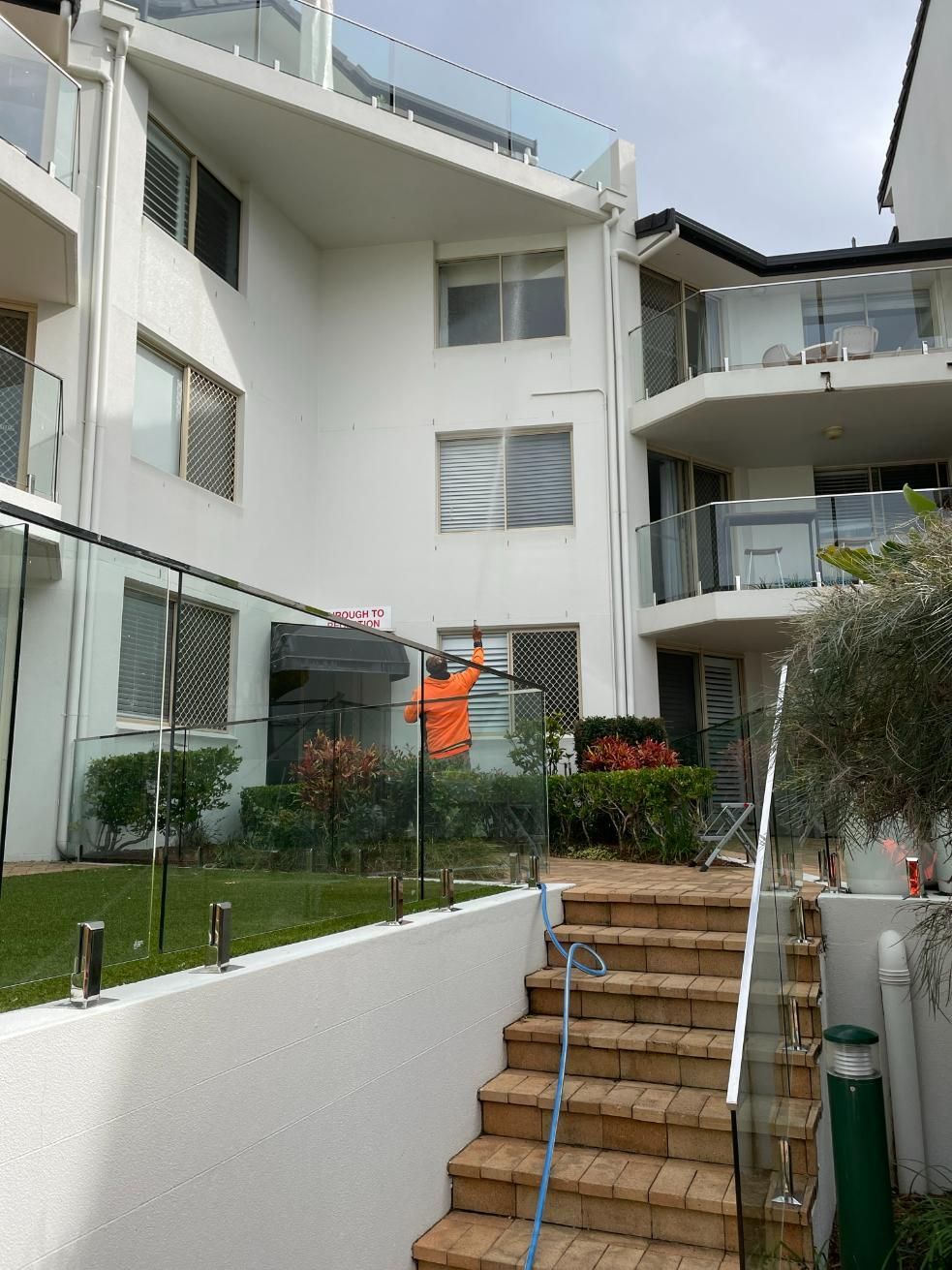 A Man Is Spraying a Building with A Hose — Hard Surface Cleaners in Melbourne, VIC