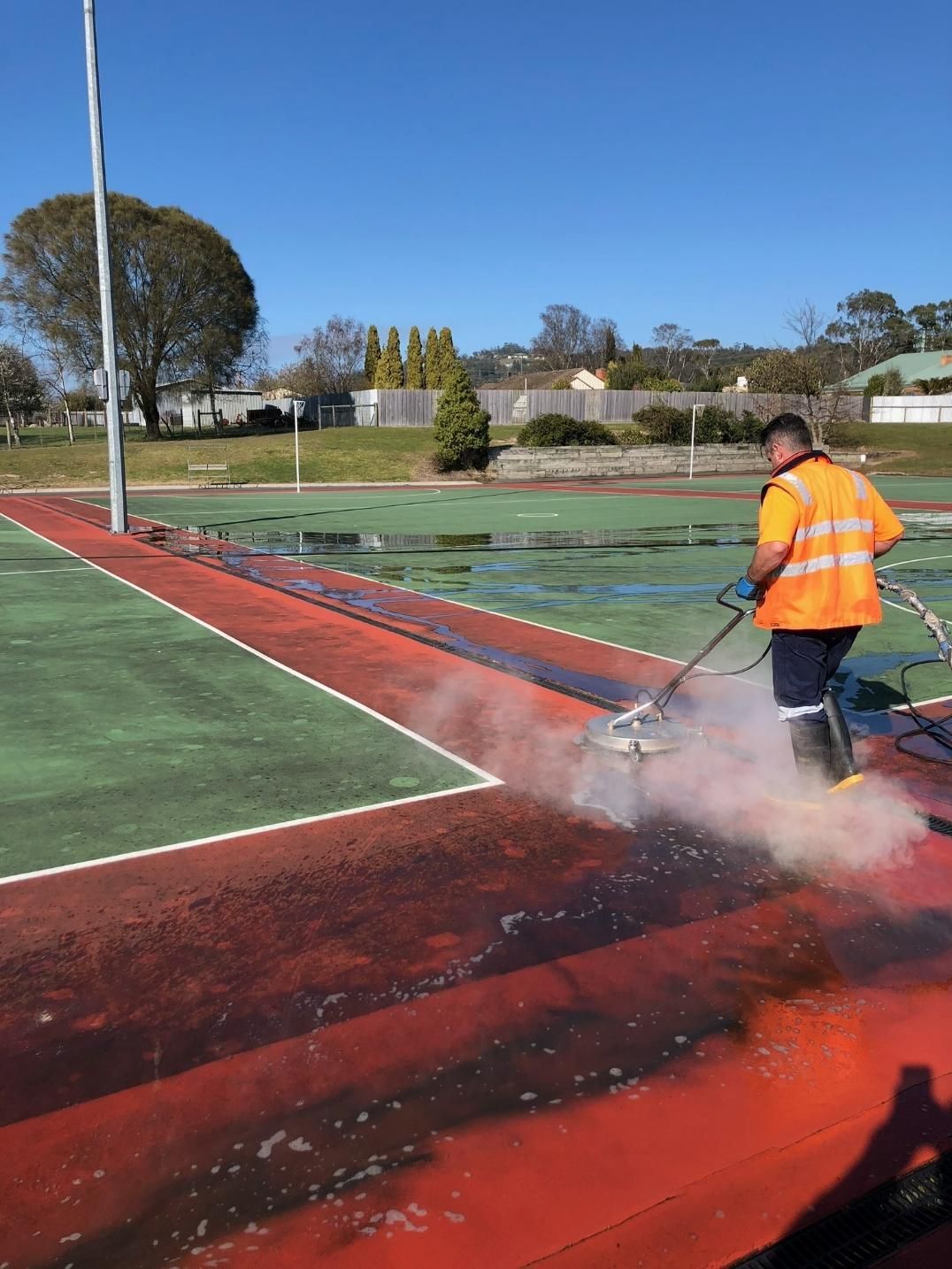A Man Is Cleaning a Tennis Court with A Machine — Hard Surface Cleaners in Clayton, VIC