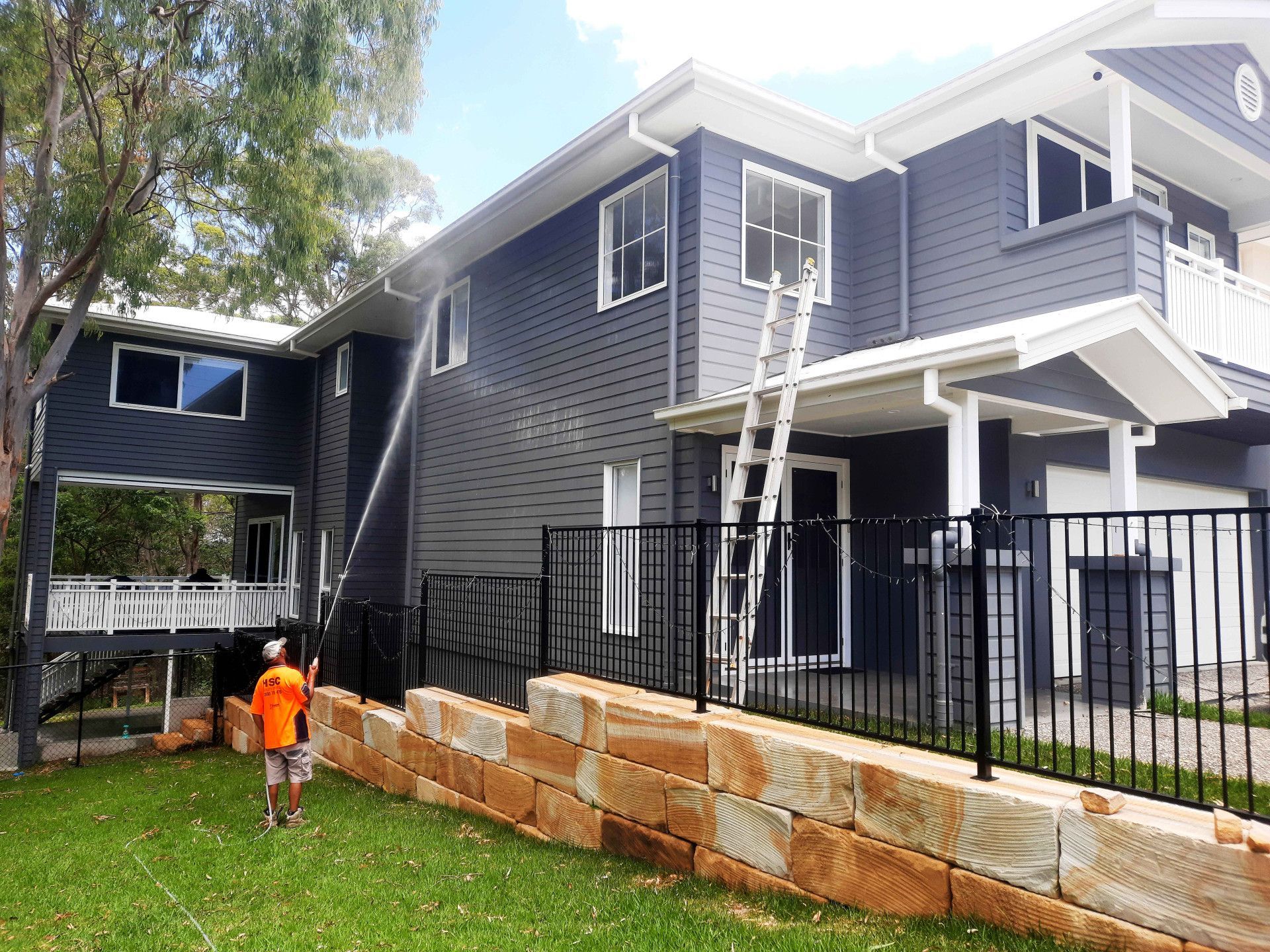 A man in an orange shirt is standing in front of a large house. — Hard Surface Cleaners in Gold Coast, QLD