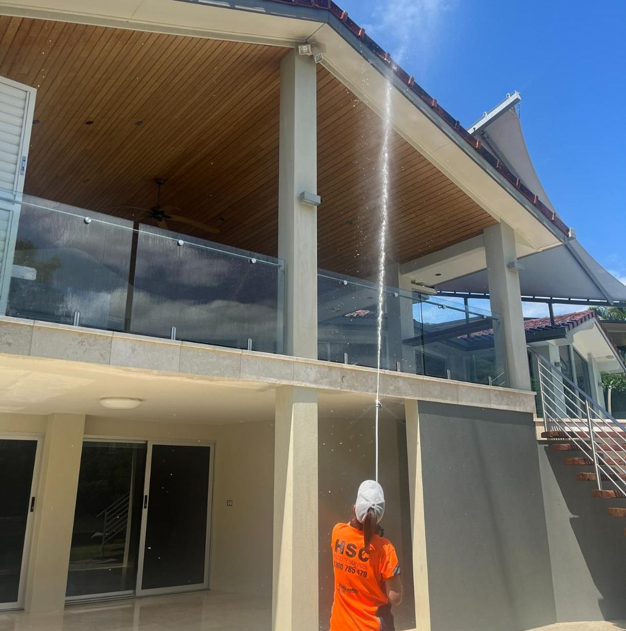 A Man Is Cleaning the Roof of A Building with A High Pressure Washer — Hard Surface Cleaners in Clayton, VIC