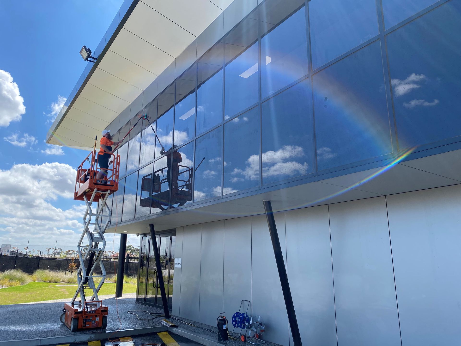 A man is cleaning the windows of a building with a rainbow in the — Hard Surface Cleaners in Gold Coast, QLDbackground.