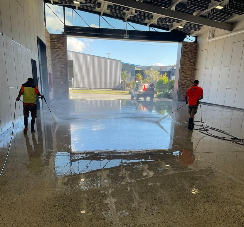 Two Men Are Cleaning the Floor of A Building with A High Pressure Washer — Hard Surface Cleaners in Clayton, VIC