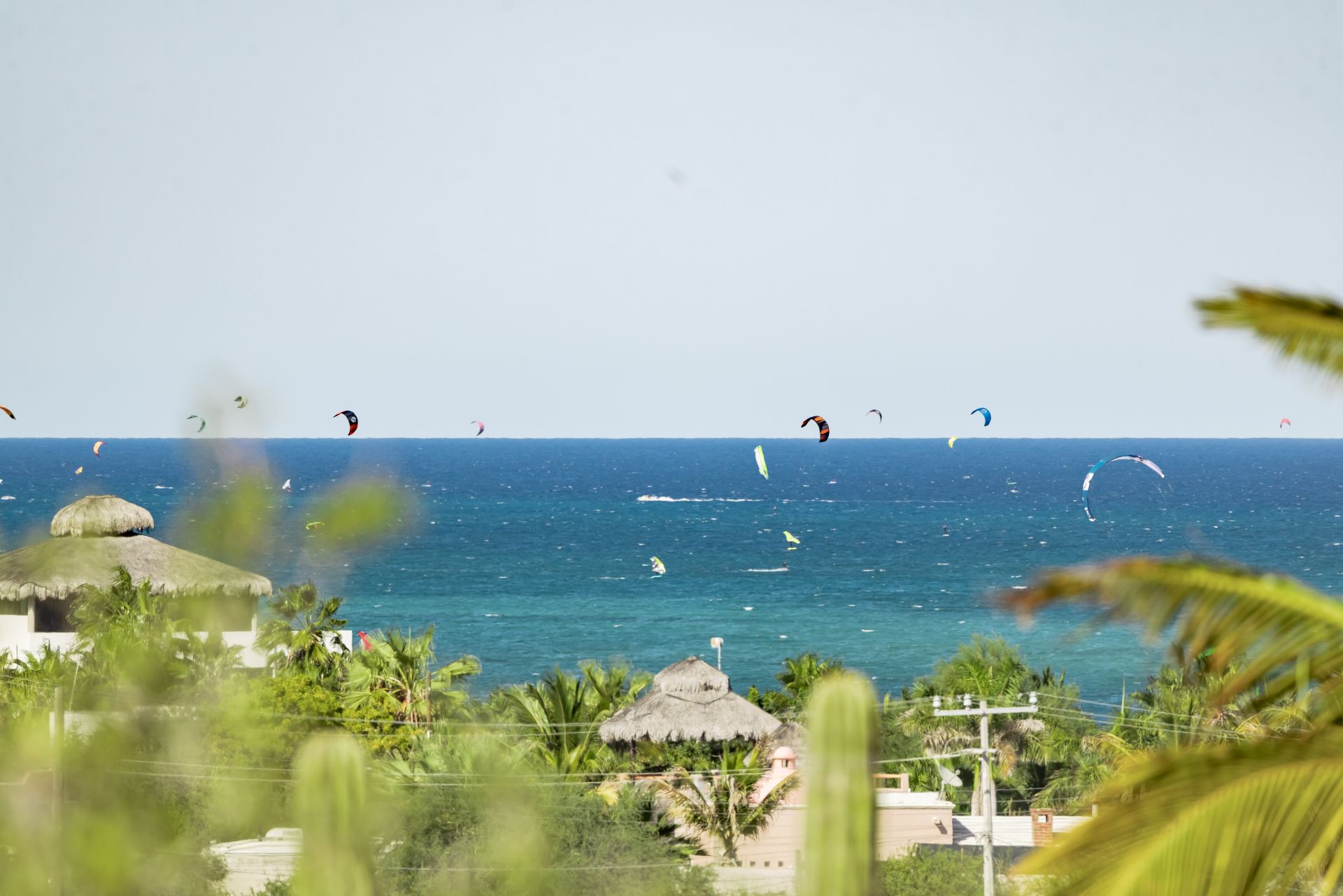 Kite surfers on the blue ocean under a clear sky; tropical buildings in the foreground.