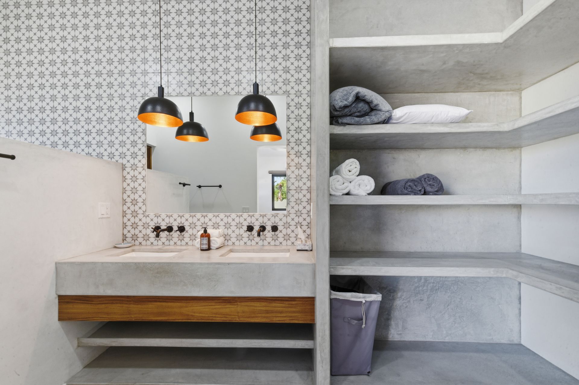 Modern bathroom with concrete vanity, patterned wall, open shelves, and pendant lights.